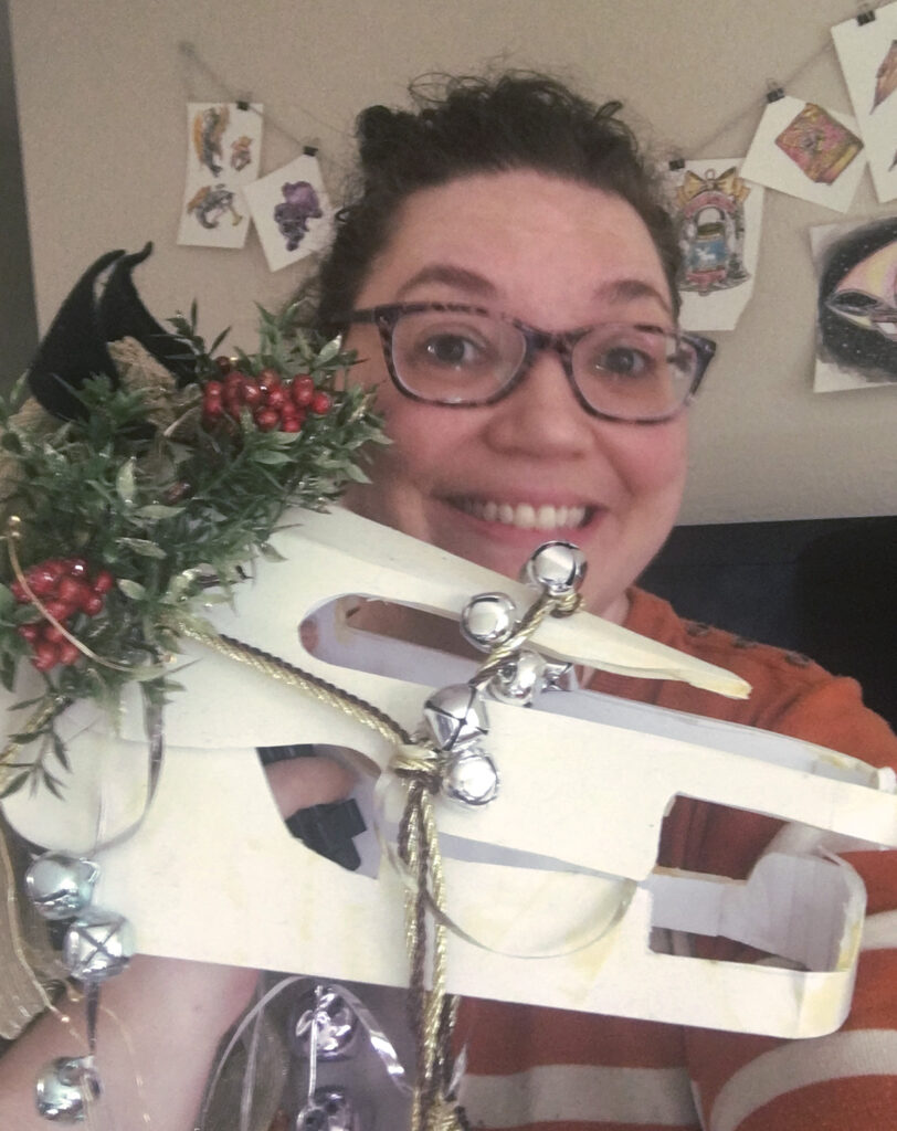 Smiling white woman in glasses shows off a papercraft horse skull decorated with ribbons and jingle bells